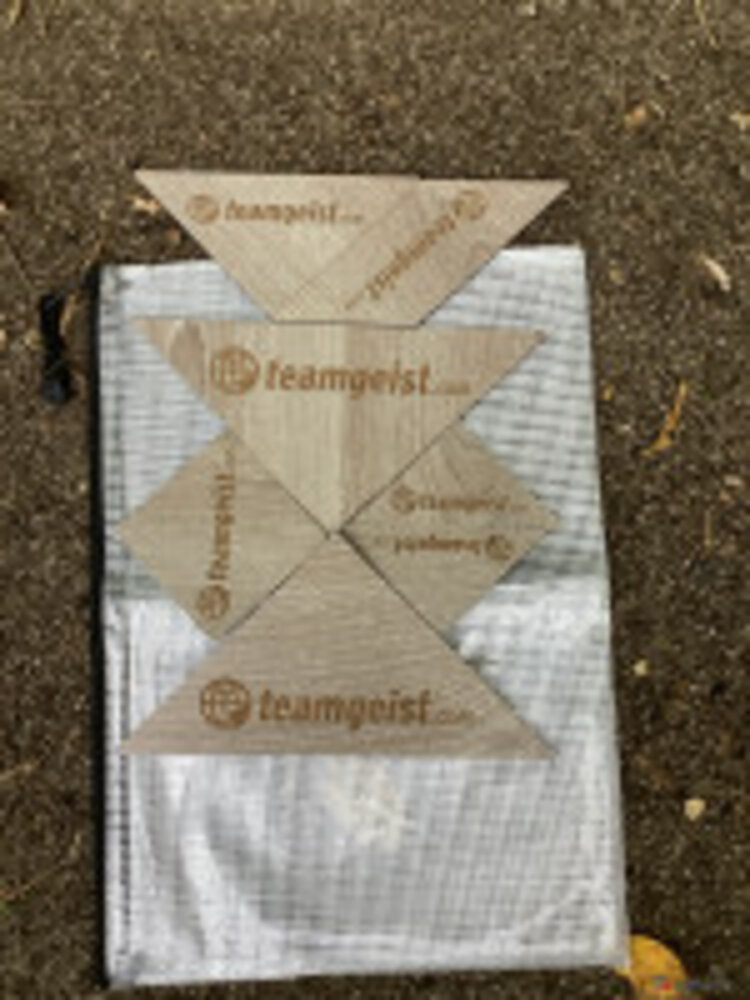 Auf einer Plastiktüte, die auf Asphalt liegt, wurden unterschiedlich große Holzdreiecke mit Aufschrift und Logo von Teamgeist positioniert.