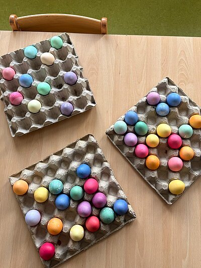 Drei große Eierschachteln mit bunt gefärbten Eiern.