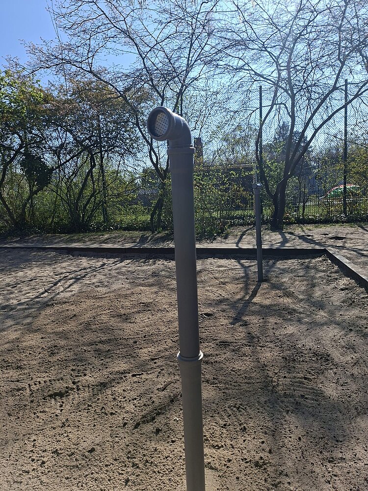 Auf einem Spielplatz ragt ein blaues Rohrtelefon aus dem Boden.