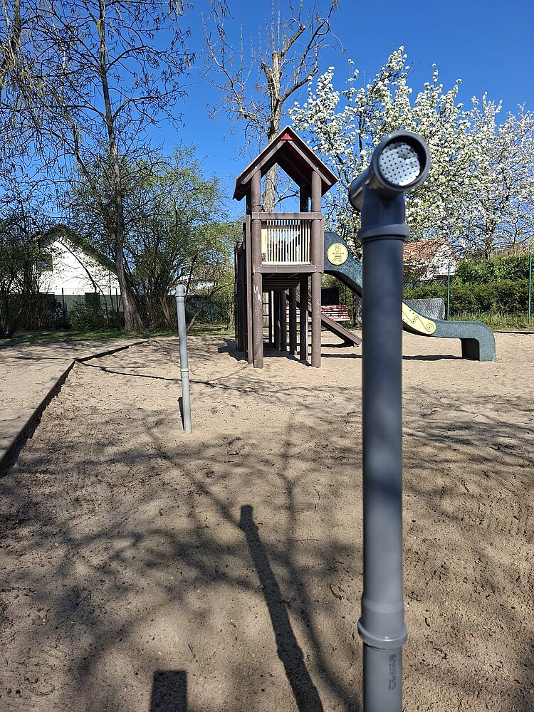 Auf einem Spielplatz ragt ein blaues Rohrtelefon aus dem Boden.