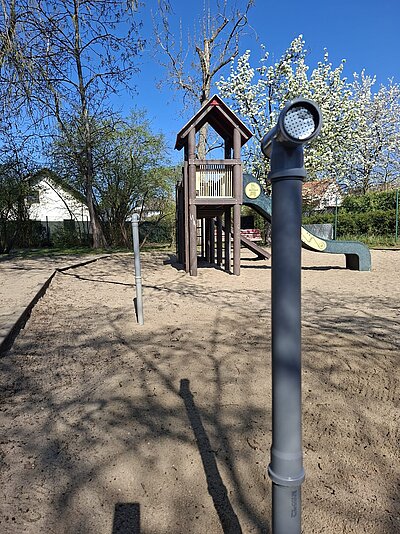 Auf einem Spielplatz ragt ein blaues Rohrtelefon aus dem Boden.