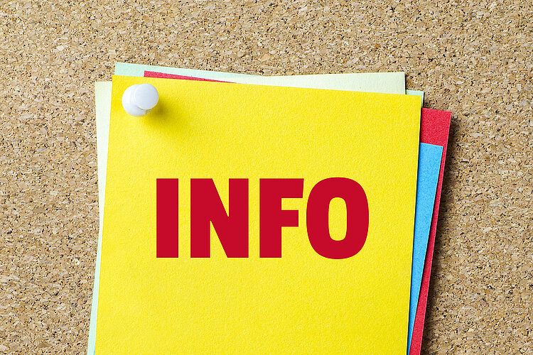 Die Aufschrift "Info" in großen roten Lettern steht auf einem gelben Zettel, der mit andern bunten Zetteln auf einer Pinwand angepinnt ist.
