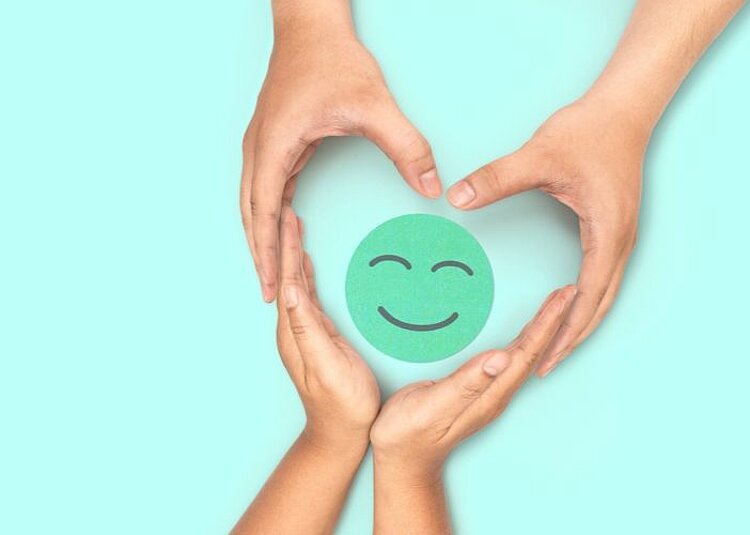 Auf einem türkisen Hintergrund liegt ein kreisrunder Smiley in einem etwas dunkleren Ton. Zwei geschwungene Handpaare umkreisen der Smiley in Herzform.