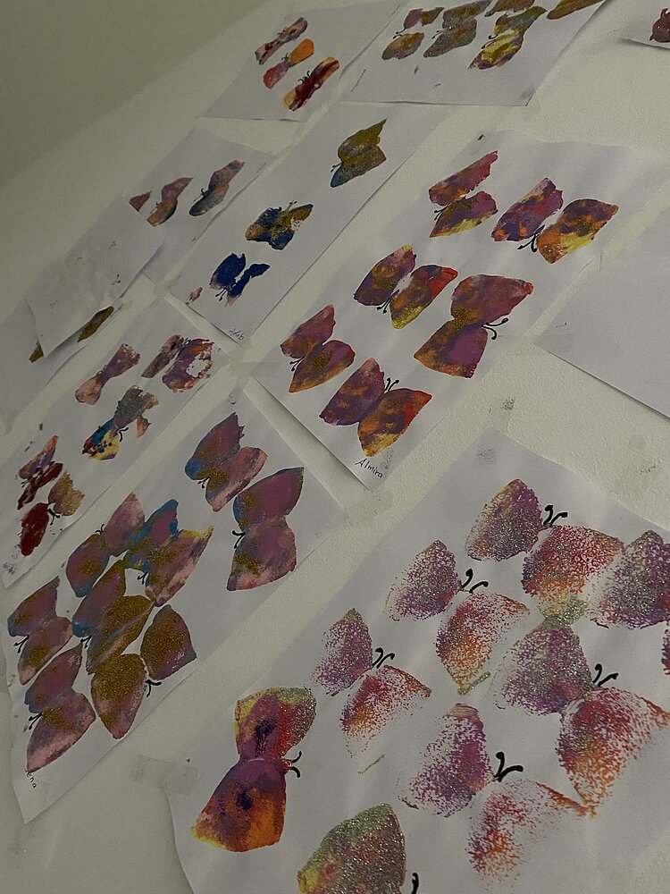 Mehrere Papierblätter mit bunt gemalten Schmetterlingen liegen nebeneinander auf einem Tisch.