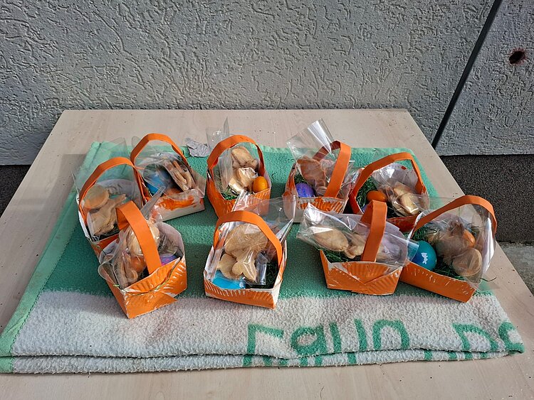 Auf einem Tisch liegt eine Decke, darauf stehen orangefarbene Osterkörbchen.